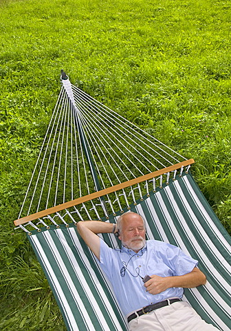 Elderly gentleman lying in a hammock and listening to music