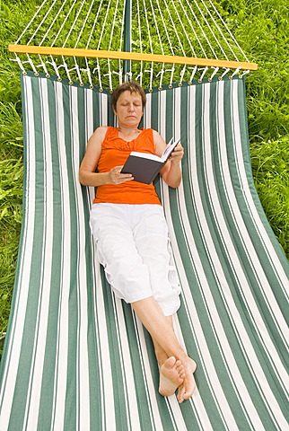 Senior woman with book lying in a hammock