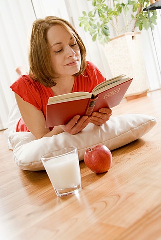 Woman lying on the parquet floor and reading a book