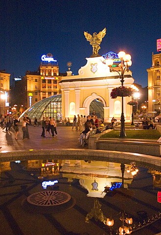 Ukraine Kiev Place of Independence people tourists visitors sit on the place with view to the PecersÂ´kyi gate with archangel Michael and fountain with water iluminated place with historical buildings of sowjetic realismn architectur national holiday 2004