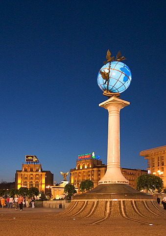 Ukraine Kiev Place of Independence people tourists visitors sit on the place with view to building of neoclassic house of labor union right and column with the world globe iluminated place with historical buildings of sowjetic realismn architectur nationa