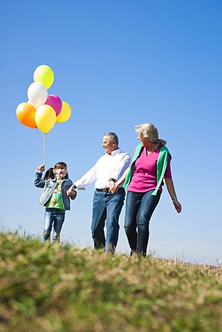 Girls holding balloons in her hand while walking with her grandparents across a meadow