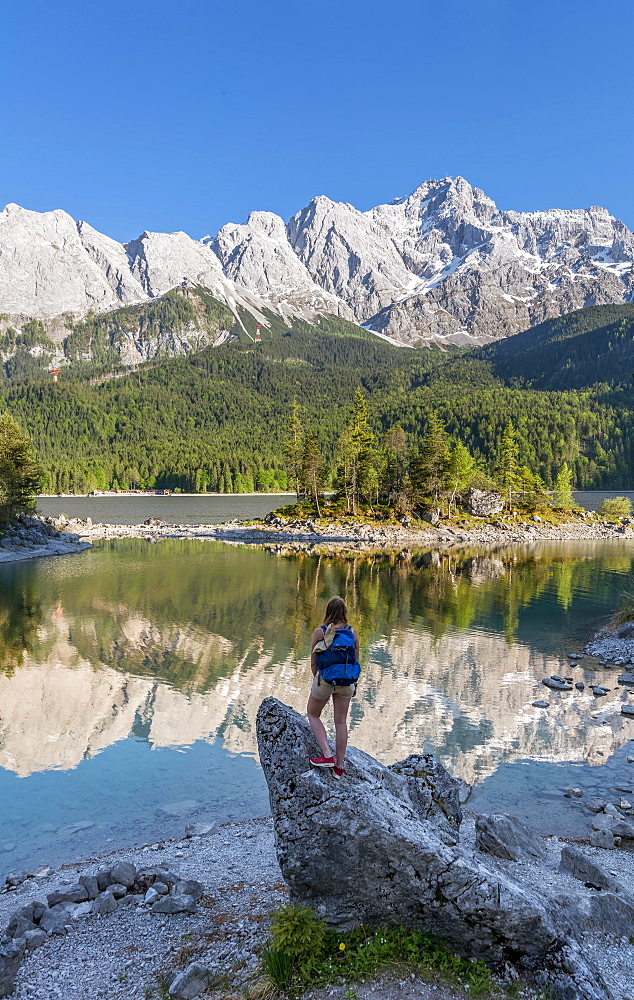 Hiker stands on rocks, looks into the distance, Lake Eibsee lake and Zugspitze, Wetterstein range, near Grainau, Upper Bavaria, Bavaria, Germany, Europe