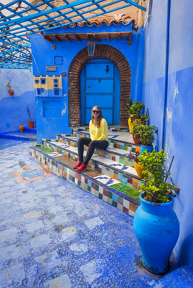 Young woman in the old town sits on a staircase, blue house walls, medina of Chefchaouen, Chaouen, Tangier-Tétouan, Kingdom of Morocco