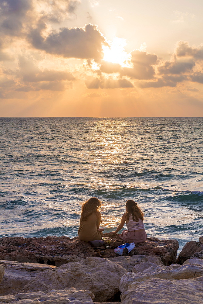 Two women sitting on rocks at sunset overlooking the sea, Tel Aviv, Israel, Asia