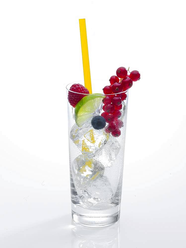 Glass prepared for cocktail, decorated with raspberry, blueberry, lime and red currant, drinking straw, ice cubes, Germany, Europe