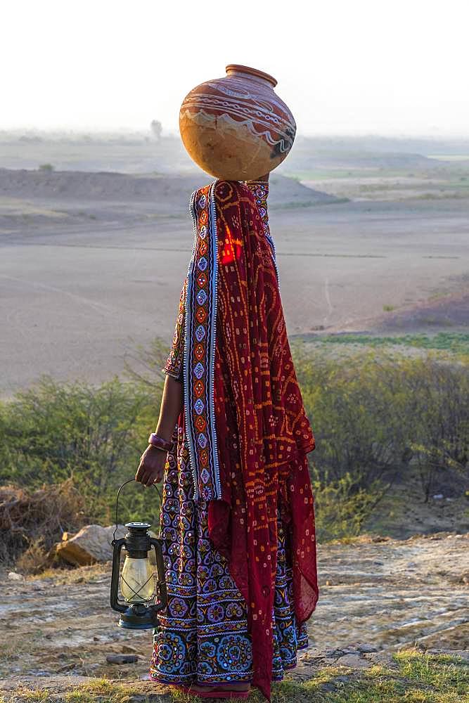 Ahir woman in traditional colorful clothes carrying water in a clay jug on her head, Great Rann of Kutch, Gujarat, India, Asia