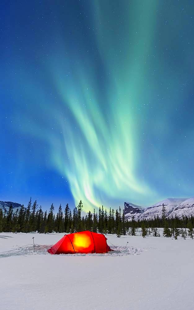 Northern Lights (Aurora borealis) above a red illuminated tent in winter, Kungsleden, Province of Lapland, Sweden, Europe