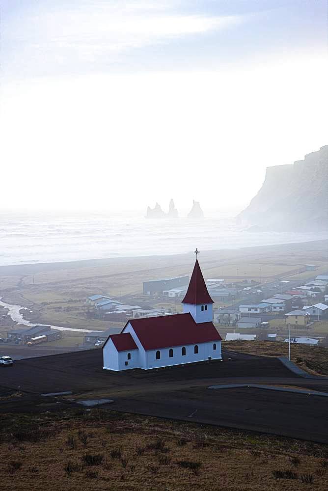 Small church with red roof, behind it the village Vik and the rocks of Reynisfjara, Sudurland, South Iceland, Iceland, Europe