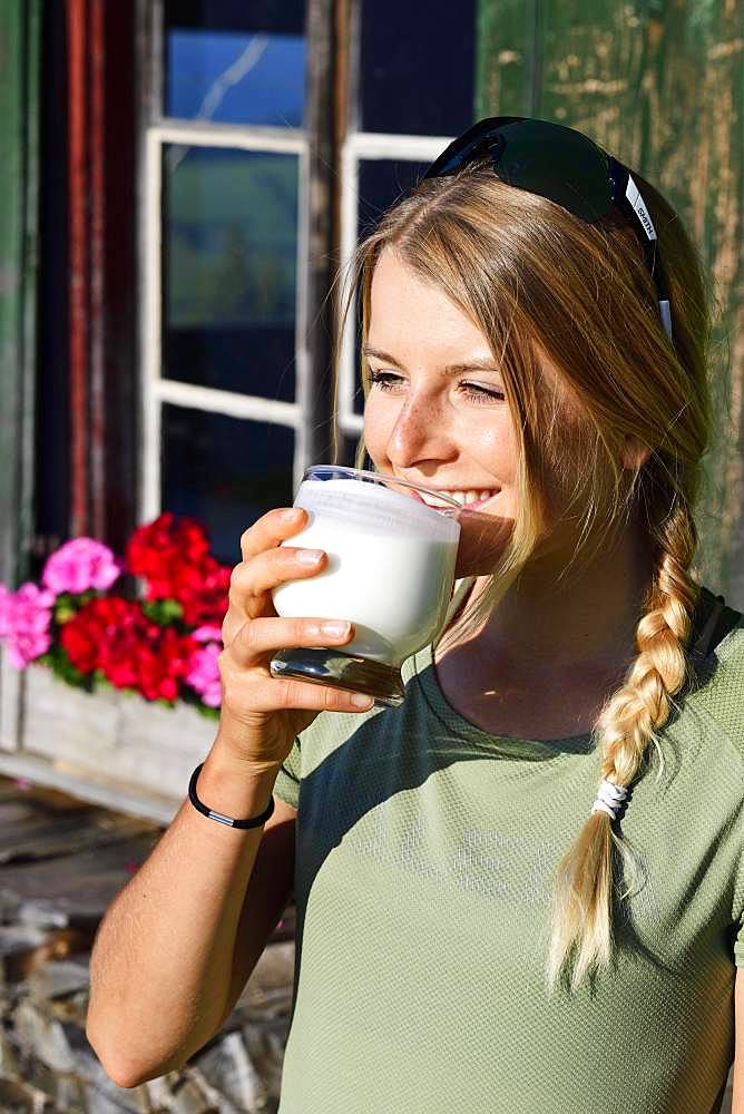 Young female hiker drinks buttermilk at the Kraftalm, Hohe Salve, Itter, Kitzbuehel Alps, Tyrol, Austria, Europe