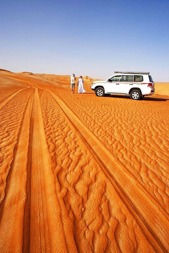 Tire tracks in the sand, tourist and Bedouin standing next to off-road vehicle, desert safari, desert Rimal Wahiba Sands, Oman, Asia