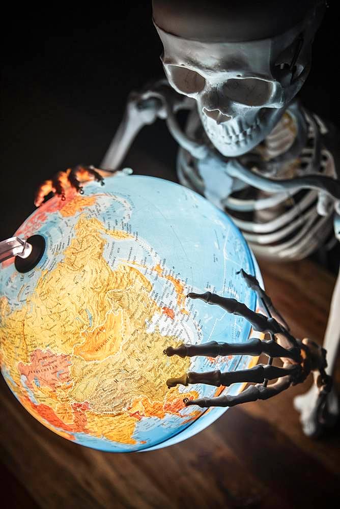 Skeleton with bony hand on globe, symbolic image of war and environmental catastrophe, Germany, Europe