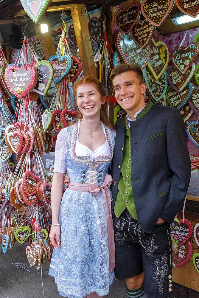 Young couple in traditional traditional traditional traditional traditional traditional traditional traditional traditional traditional costume in front of gingerbread hearts, gingerbread stand, Wiesn, Wiesn, Oktoberfest, Munich, Upper Bavaria, Bavaria, Germany, Europe