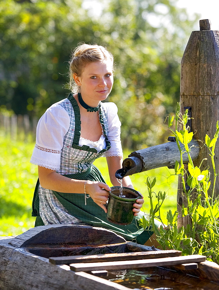 Young woman in dirndl fills a water jug at the well, 19 years, Upper Austria, Austria, Europe