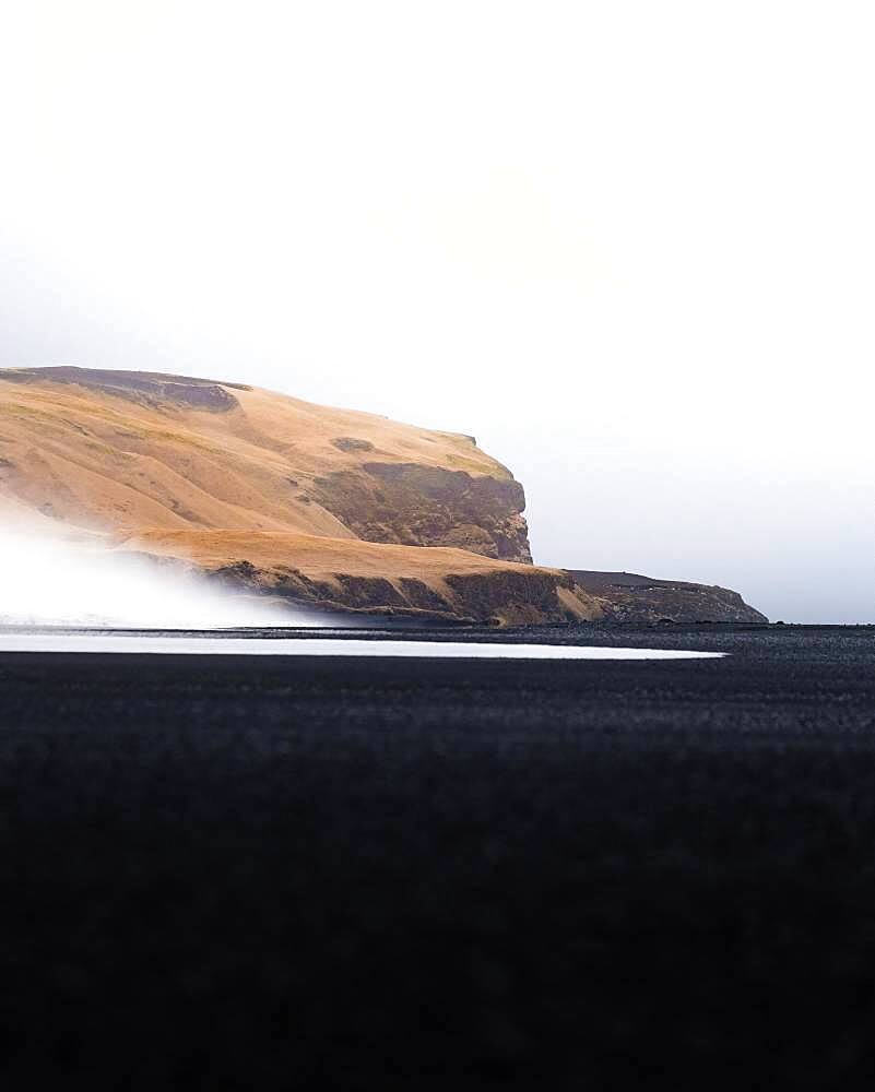 Yellow grassy mountain with black sand and waves in the foreground, Vik Beach, Iceland, Europe