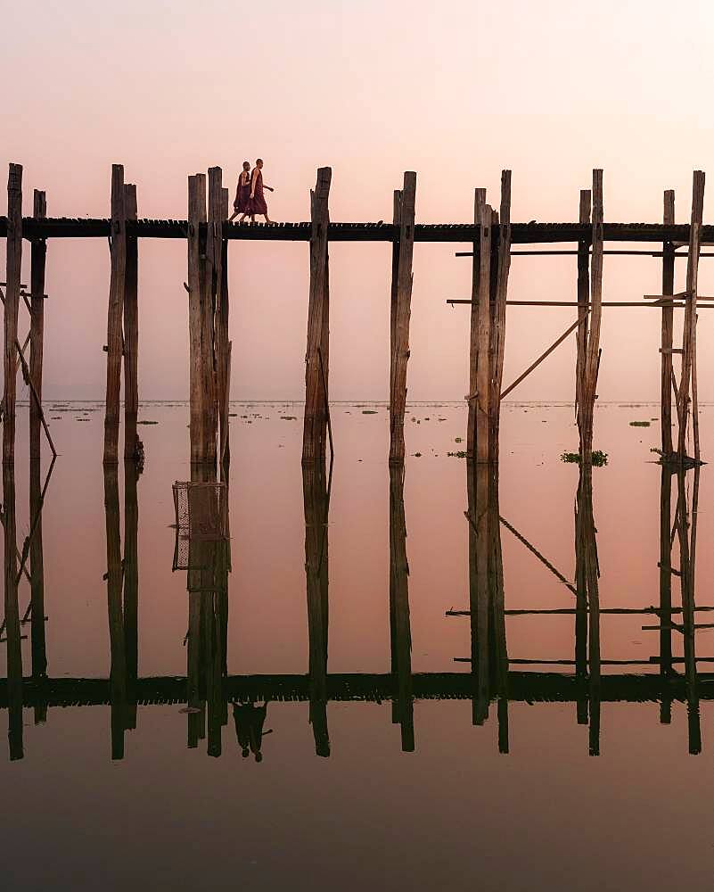 Buddhist monks walk across the U-leg bridge in red robes as the sun rises, Mandalay, Myanmar, Asia