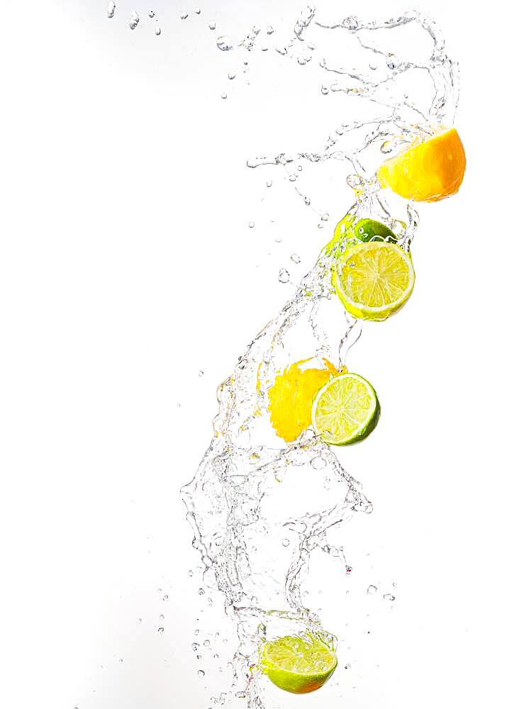 Fresh limes and lemons with water splashes in the air, white background