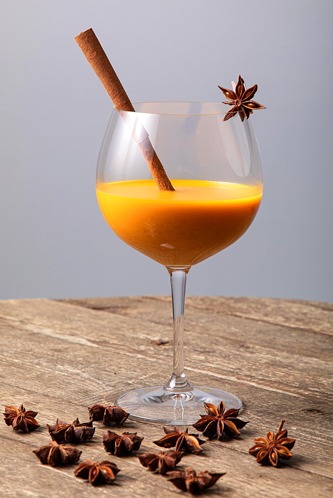 Orange fruity cocktail with cinnamon stick and star anise in a glass, on a wooden table