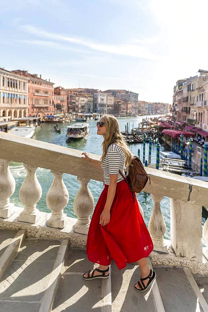 Young woman with red skirt walks over a bridge at the Grand Canal, Rialto Bridge, Venice, Veneto, Italy, Europe