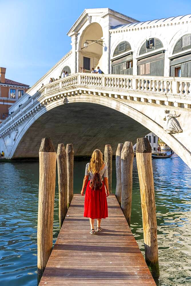 Young woman with red dress at a pier with boats, Grand Canal, Rialto Bridge, Venice, Veneto, Italy, Europe