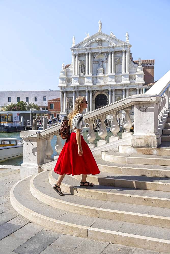 Young woman with red skirt walks over a bridge at the Grand Canal, Church of Santa Maria di Nazareth, Ponte degli Scalzi, Venice, Veneto, Italy, Europe