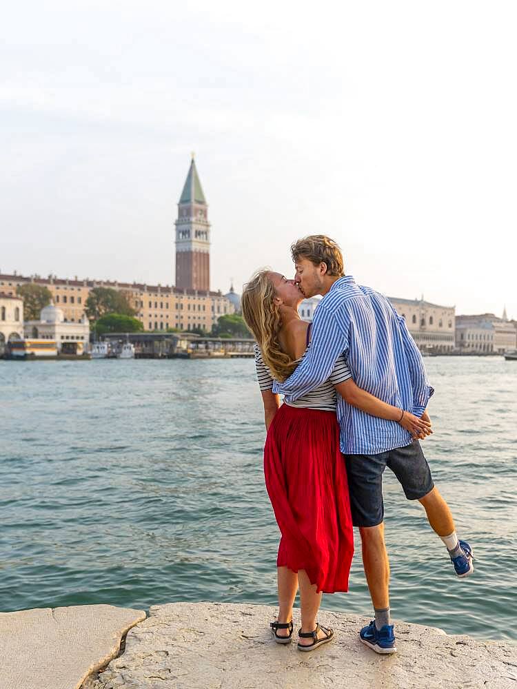 Young couple in love standing by the sea enjoying view of St. Mark's Square with Campanile di San Marco, Venice, Veneto, Italy, Europe