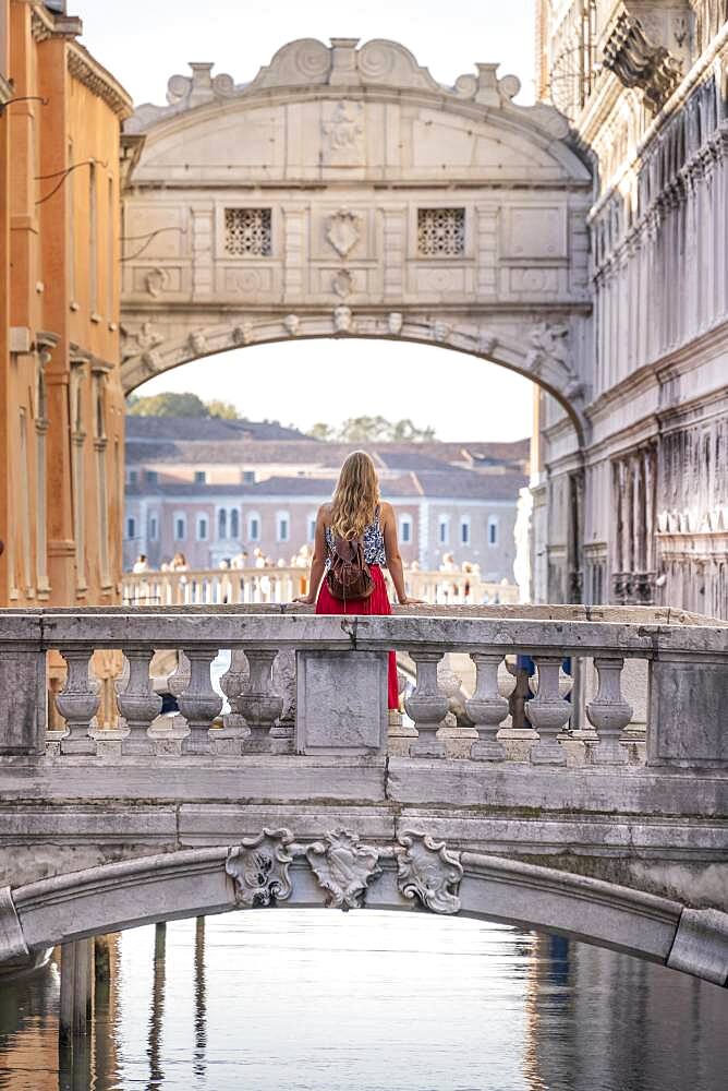 Young woman with red skirt, tourist leaning on bridge railing, bridge over Rio di Palazzo, behind Bridge of Sighs, Venice, Veneto, Italy, Europe