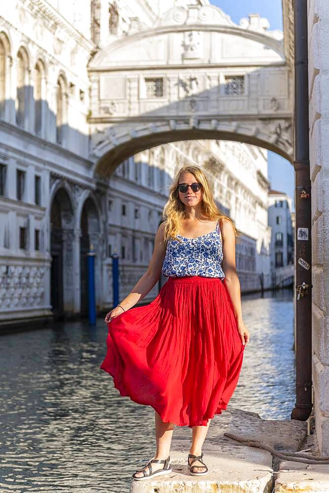 Young woman with red skirt, tourist at the canal Rio di Palazzo, behind Bridge of Sighs, Venice, Veneto, Italy, Europe