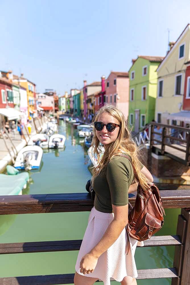 Young woman in front of colorful houses, canal with boats and colorful house facades, Burano Island, Venice, Veneto, Italy, Europe