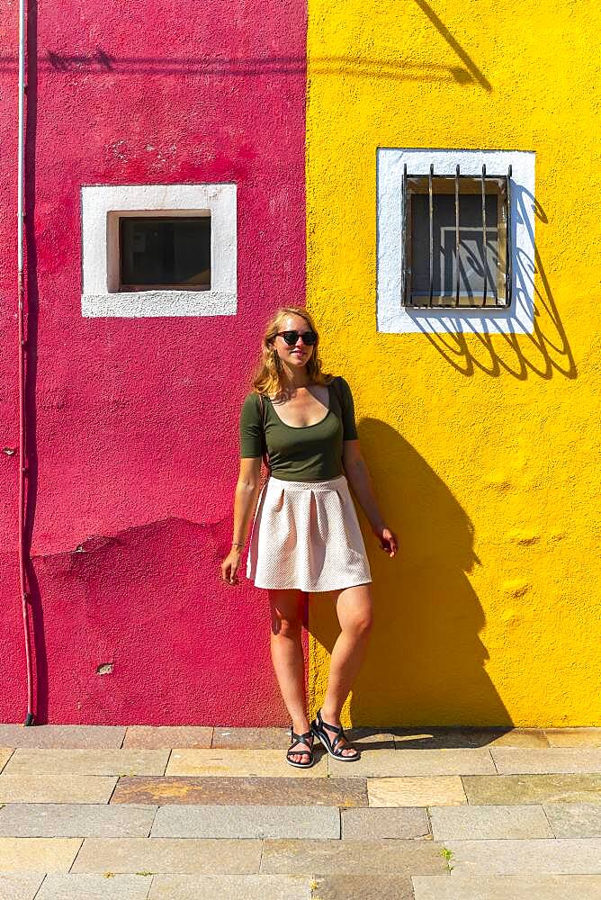 Young woman in front of colorful house, red and yellow house facade, Burano Island, Venice, Veneto, Italy, Europe