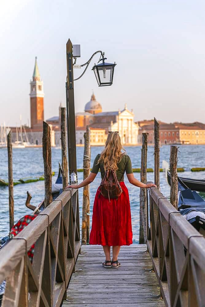 Young woman with red dress on a jetty, behind church San Giorgio Maggiore, Venice, Veneto, Italy, Europe