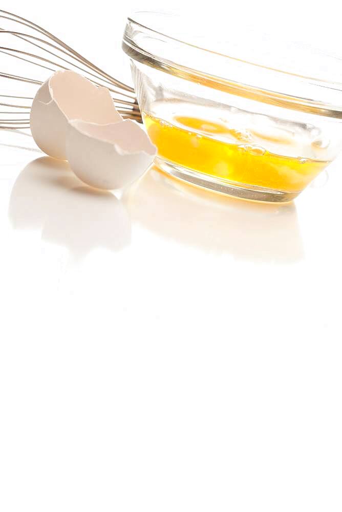 Hand mixer with eggs in a glass bowl on a reflective white background