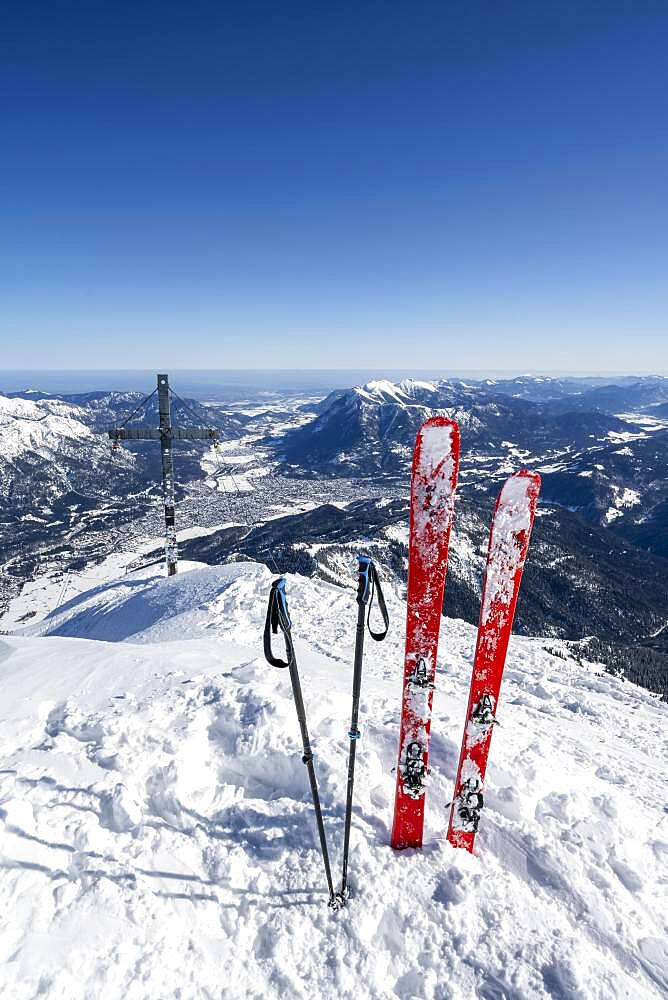 Ski stuck in snow, Alpspitz summit with summit cross, ski tour to Alpspitze, view to Garmisch-Patenkirchen, Wetterstein mountains with snow in winter, Garmisch-Partenkirchen, Bavaria, Germany, Europe