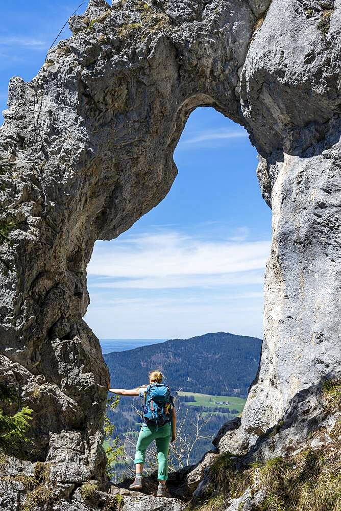 Hiker standing in the rock gate Breitensteinfensterl with view of high fog over the valley, hiking trail to Breitenstein, Fischbachau, Bavaria, Germany, Europe