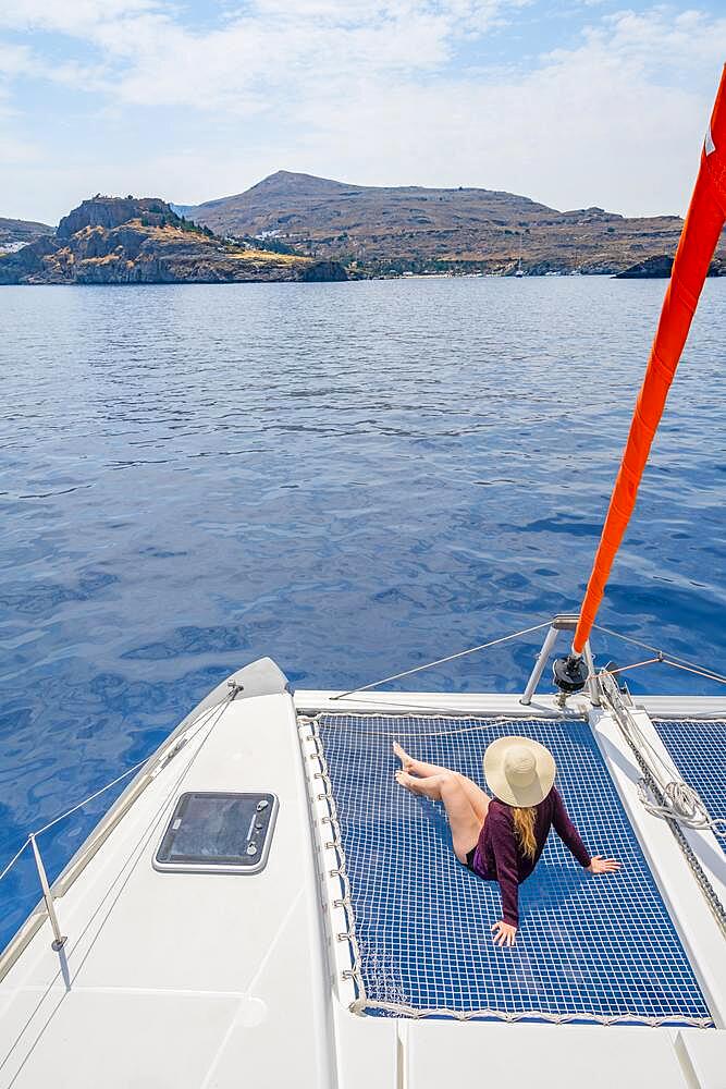 Young woman with hat sitting in the net of a sailing catamaran, sailing trip, Rhodes, Dodecanese, Greece, Europe