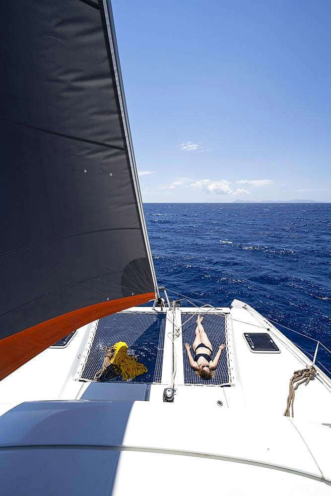 Young woman lying in the net on the deck of a sailing catamaran, headsail, While sailing a sailing catamaran, Sailing trip, Dodecanese, Greece, Europe