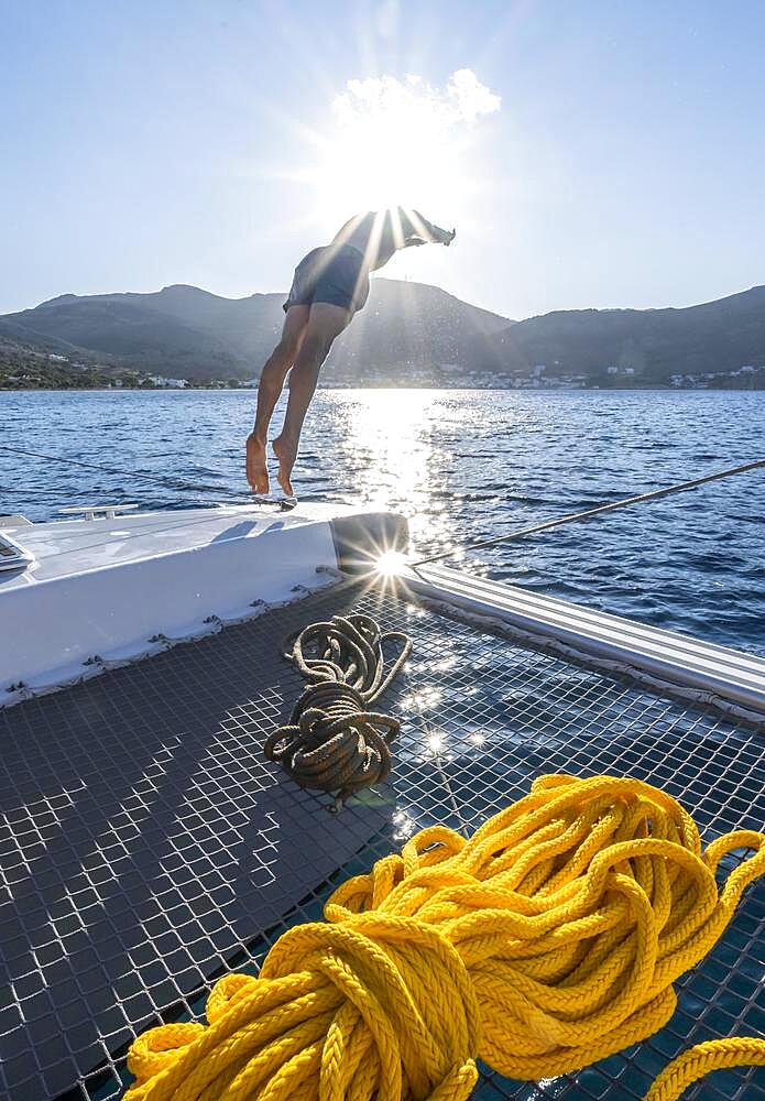 Young man jumps into the water, ropes on a sailing catamaran, Sun Star, sailing trip, Tilos, Dodecanese, Greece, Europe