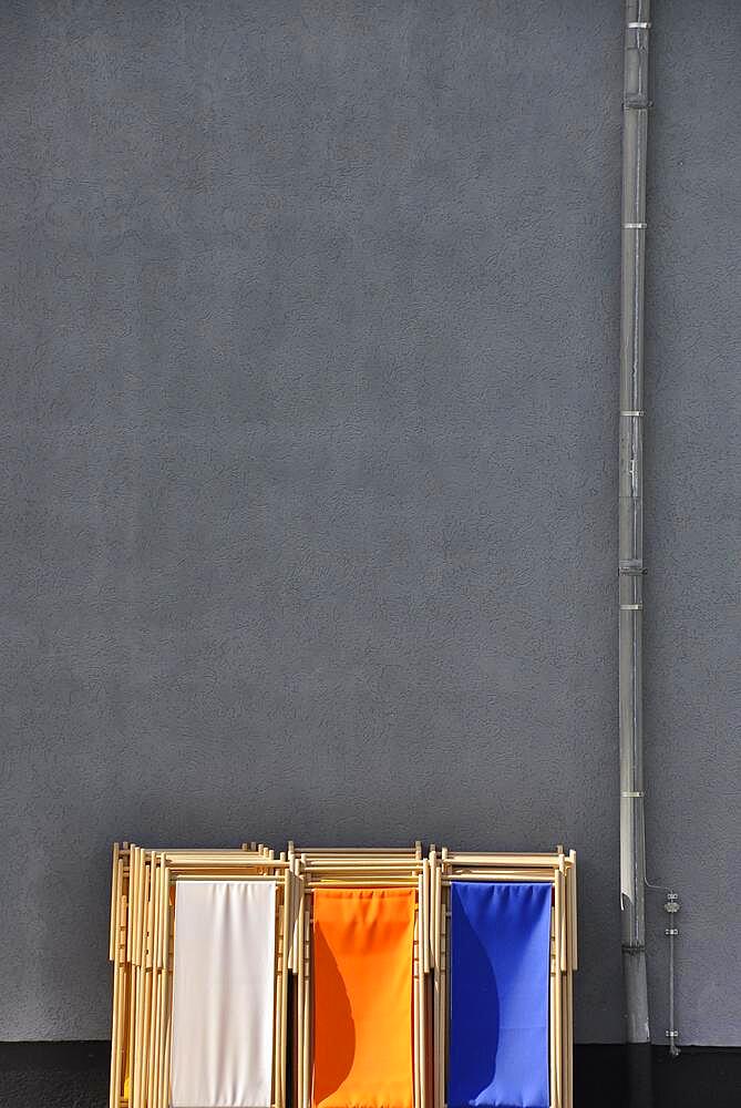 Grey wall with downpipe from gutter and coloured deck chairs in park, Cologne, Germany, Europe