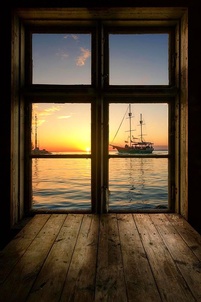 Great view from a wooden window with a wooden table, onto a lake with a sailboat. The boat is sailing into the sunset. Siofik, Balaton, Lake Balaton, Hungary, Europe