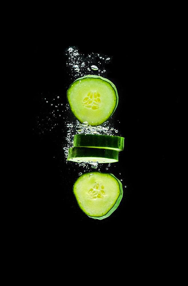 Sliced bio cucumber splashing water isolated on black background, Skin moisturizing cosmetics concept