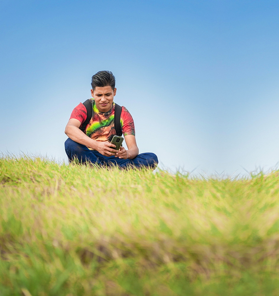 Backpacker with phone on top of a hill, a man sitting on the grass with his cell phone