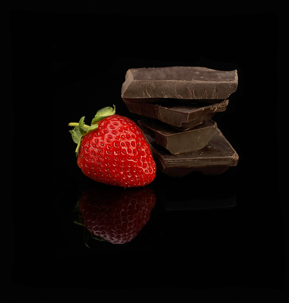 Fresh vivid colored strawberry and broken chocolate bar over black background