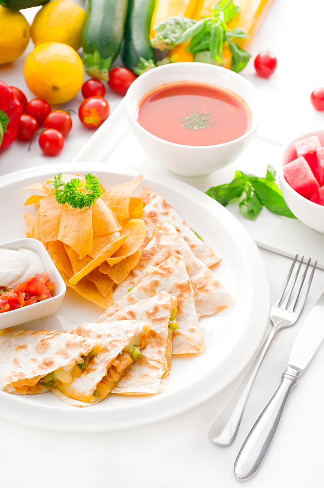 Original Mexican quesadilla de pollo with nachos served with gazpacho soup and watermelon, with fresh vegetables on background