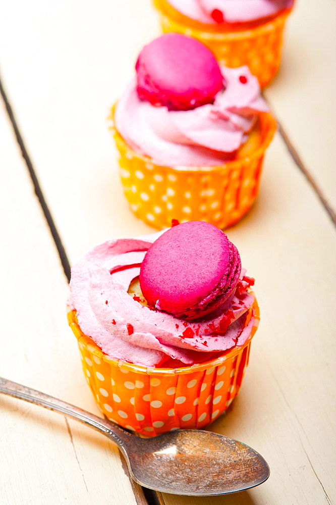 Fresh pink berry cream cupcake with macaroon on top over rustic wood table