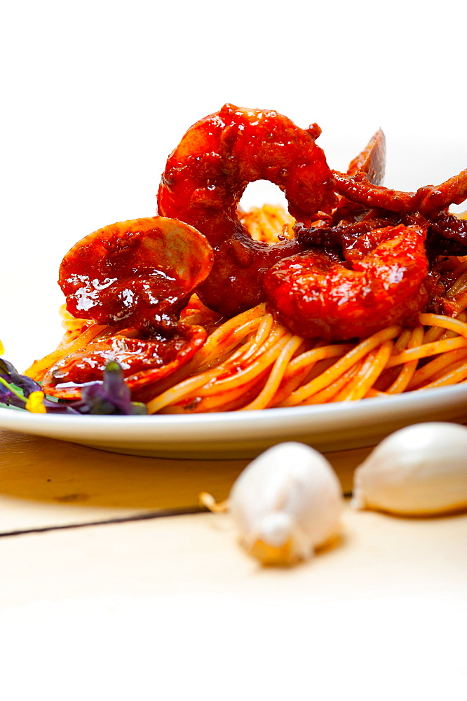 Italian seafood spaghetti pasta on red tomato sauce over white rustic wood table