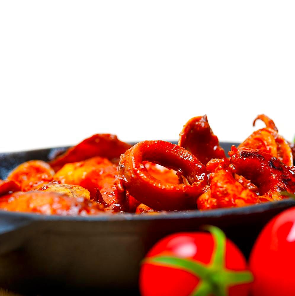 Fresh seafood stew prepared on an iron skillet ove white rustic wood table