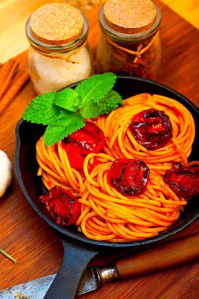 Italian spaghetti pasta and tomato with mint leaves on iron skillet over wood board