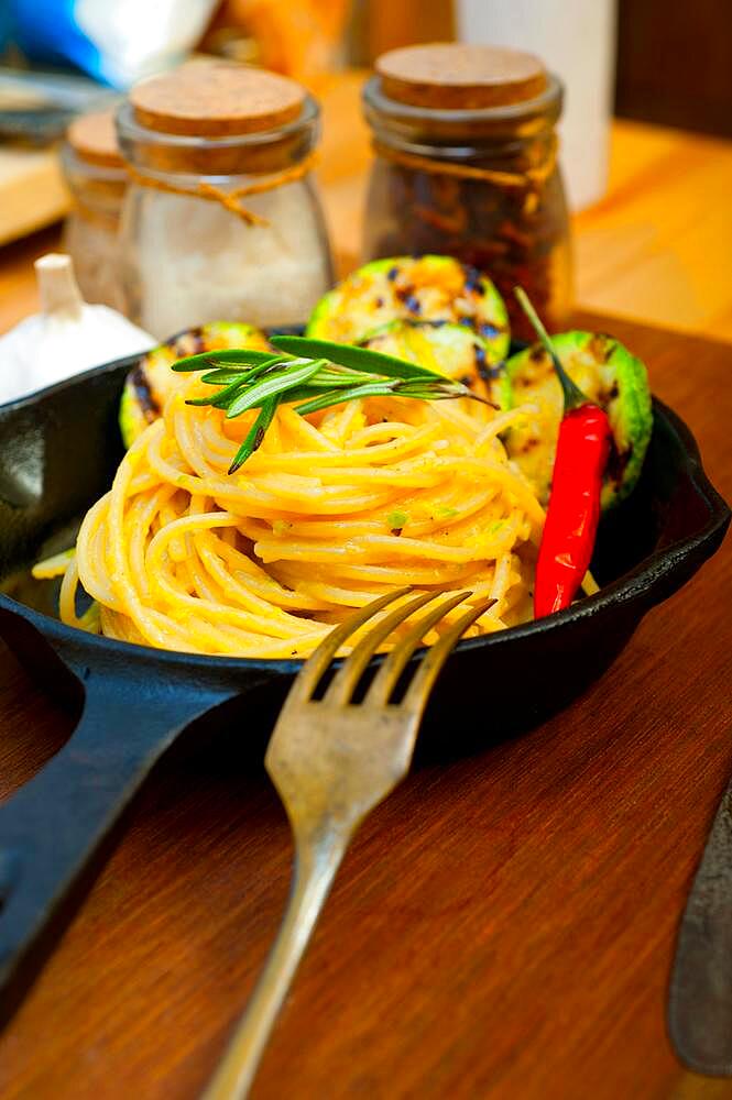 Italian spaghetti pasta with zucchini sauce on iron skillet over wood board