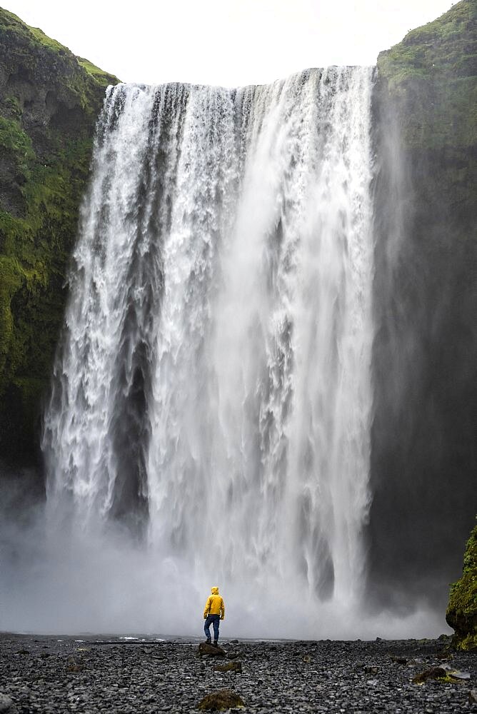 Man in front of large waterfall, Skogafoss, South Iceland, Iceland, Europe