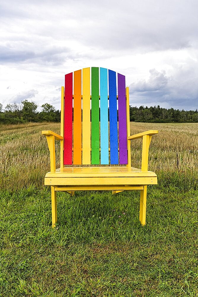 Yellow wooden chair, back painted in rainbow colours, standing in a meadow, oversized, dreary, rainy weather, Gotland Island, Sweden, Europe